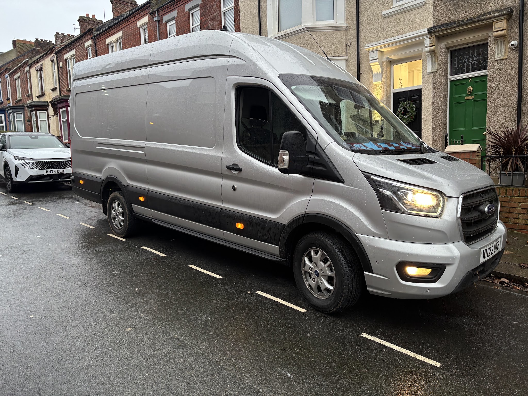 A large silver high-roof Ford Transit van parked on a terraced street