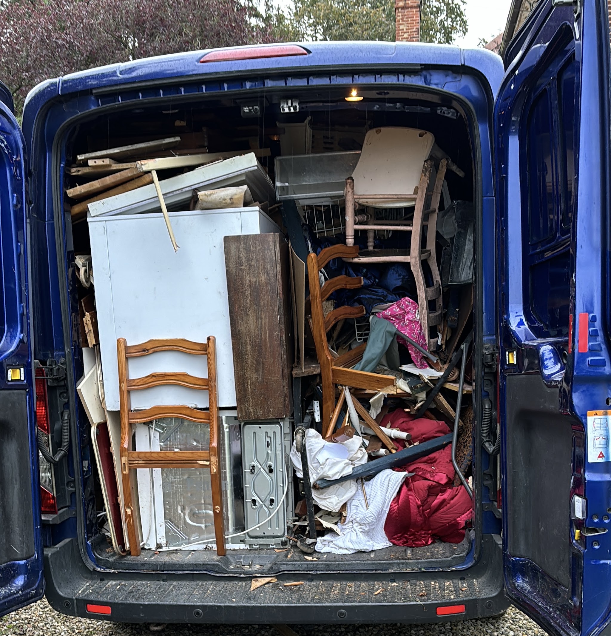 The back of a blue van packed full of chairs, a fridge, timber, bedding and household junk