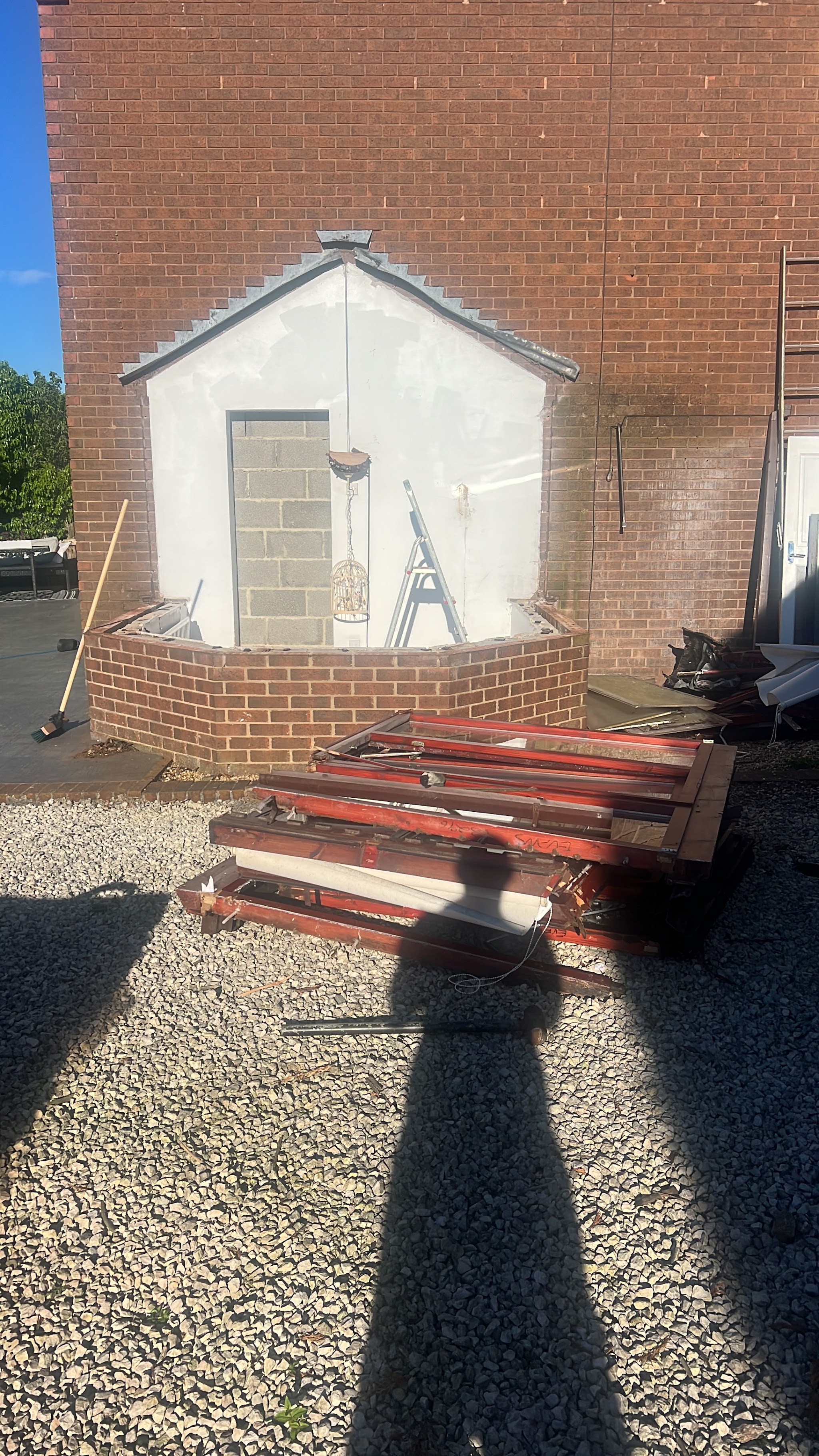 Old wooden window frames stacked on a gravel drive after being taken out