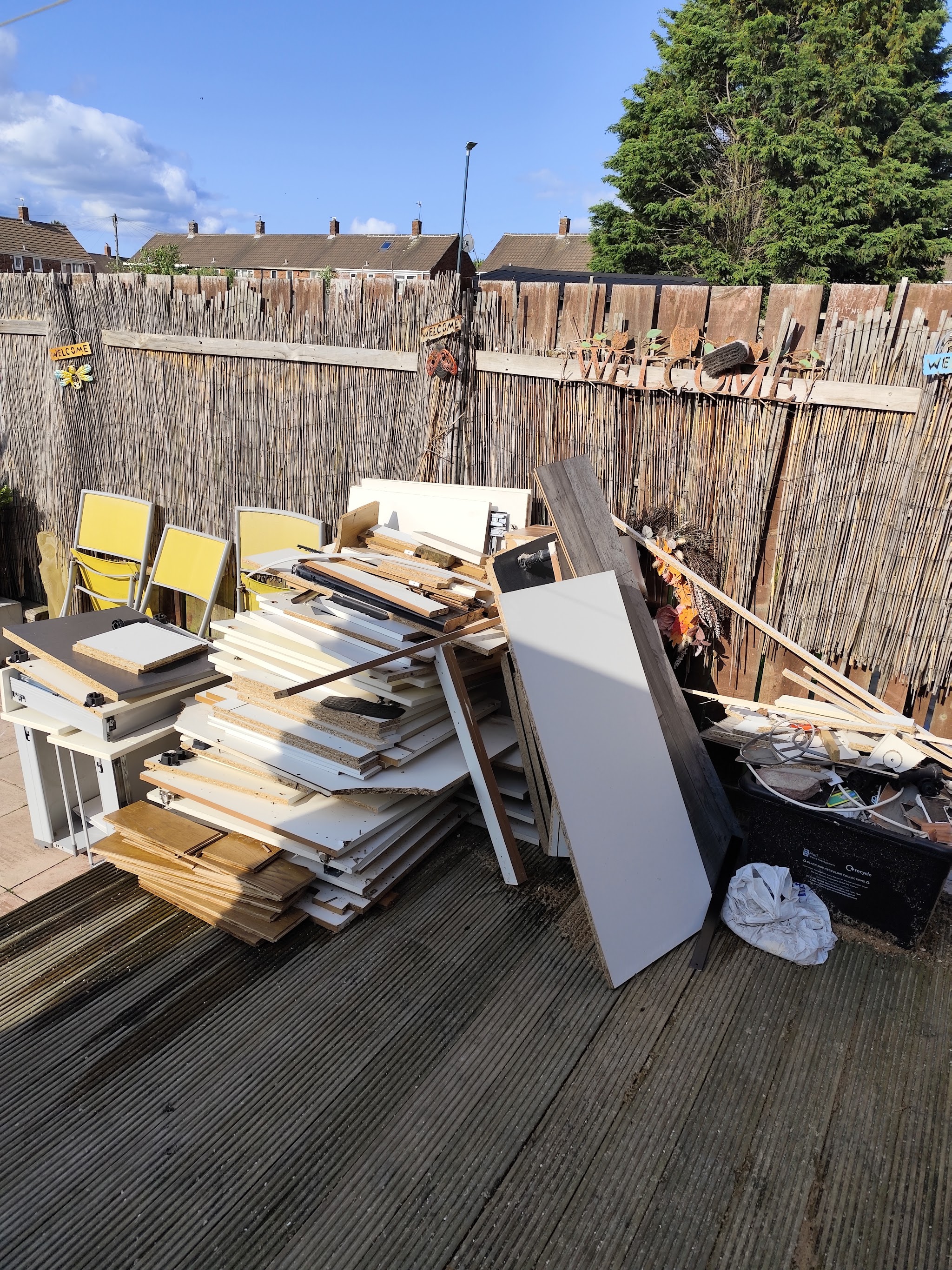 A large pile of old kitchen units and chipboard panels on garden decking