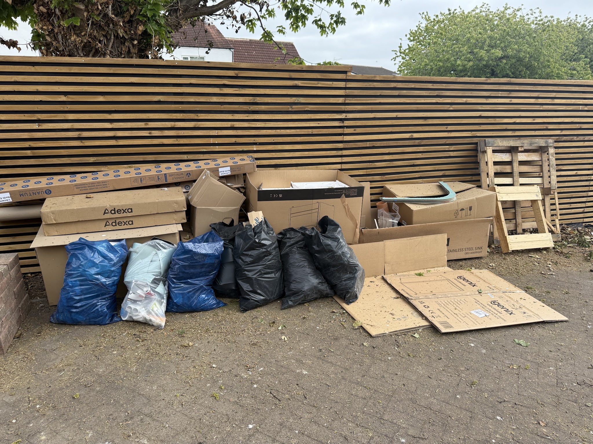Cardboard boxes, packaging and full rubbish bags lined up along a fence